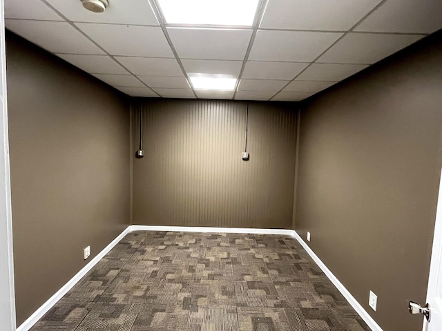 finished basement with a paneled ceiling, dark colored carpet, and baseboards