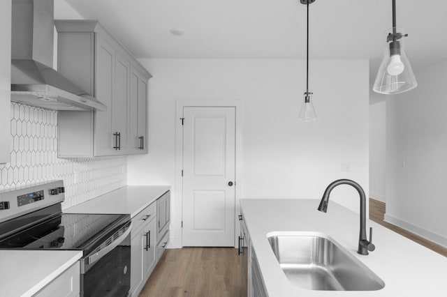 kitchen with wall chimney exhaust hood, wood finished floors, stainless steel electric range, light countertops, and a sink