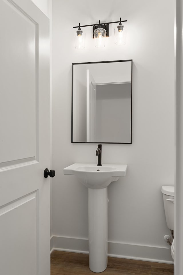 half bath featuring baseboards, toilet, and wood finished floors