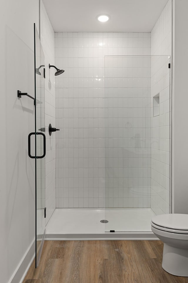 full bath with toilet, a stall shower, and wood finished floors