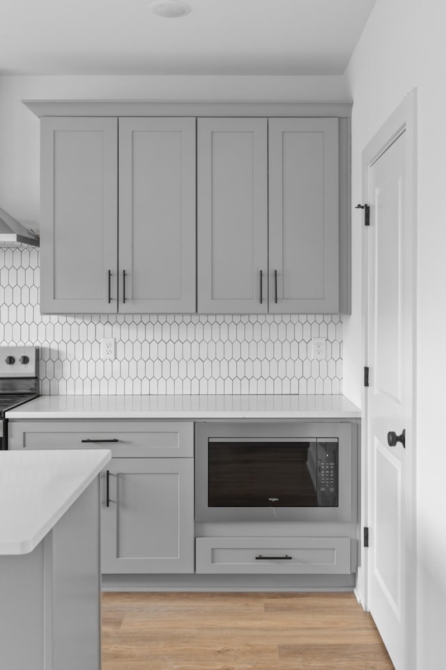 interior details featuring decorative backsplash, electric stove, built in microwave, gray cabinets, and light countertops