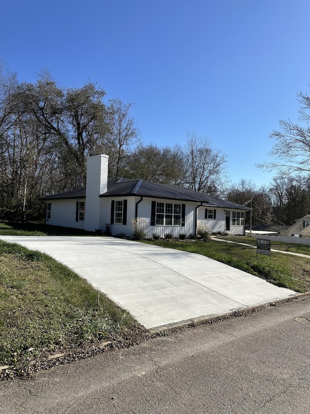 ranch-style home featuring driveway, a chimney, and a front lawn
