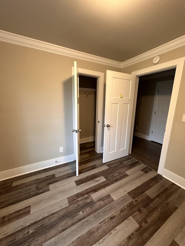 unfurnished bedroom featuring a closet, baseboards, ornamental molding, and dark wood finished floors
