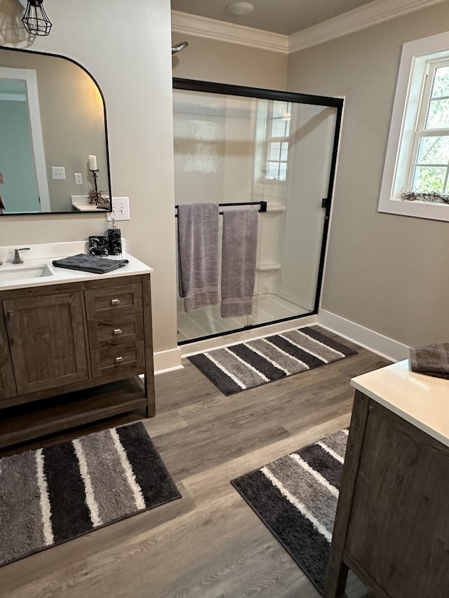 bathroom with a sink, wood finished floors, a shower stall, crown molding, and double vanity