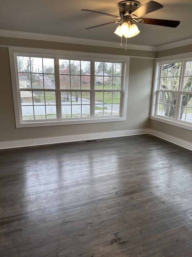 empty room featuring crown molding, dark wood-style floors, baseboards, and visible vents