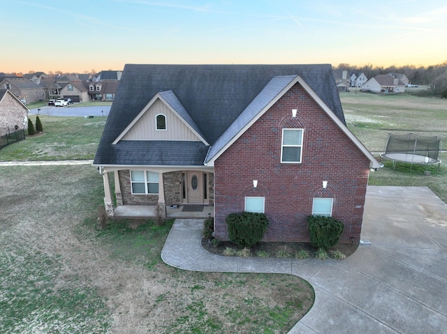 view of front facade featuring roof with shingles, brick siding, a trampoline, and a lawn