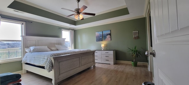 bedroom with visible vents, a raised ceiling, wood finished floors, and ornamental molding