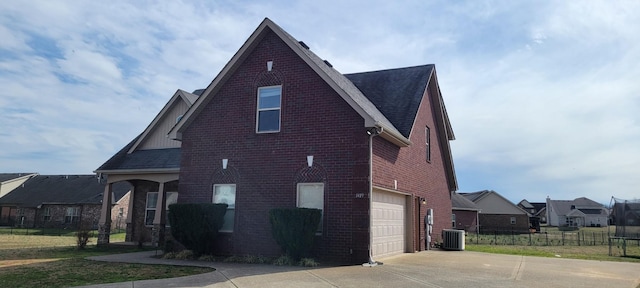 view of home's exterior with fence, driveway, an attached garage, central air condition unit, and brick siding