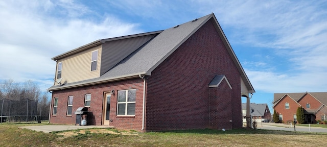 exterior space featuring a trampoline, a patio, brick siding, and a lawn