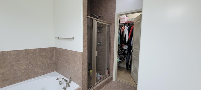 bathroom with tile patterned floors, a spacious closet, a shower stall, and a tub with jets