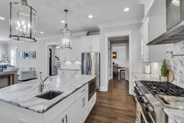 kitchen featuring a chandelier, a sink, open floor plan, appliances with stainless steel finishes, and wall chimney exhaust hood