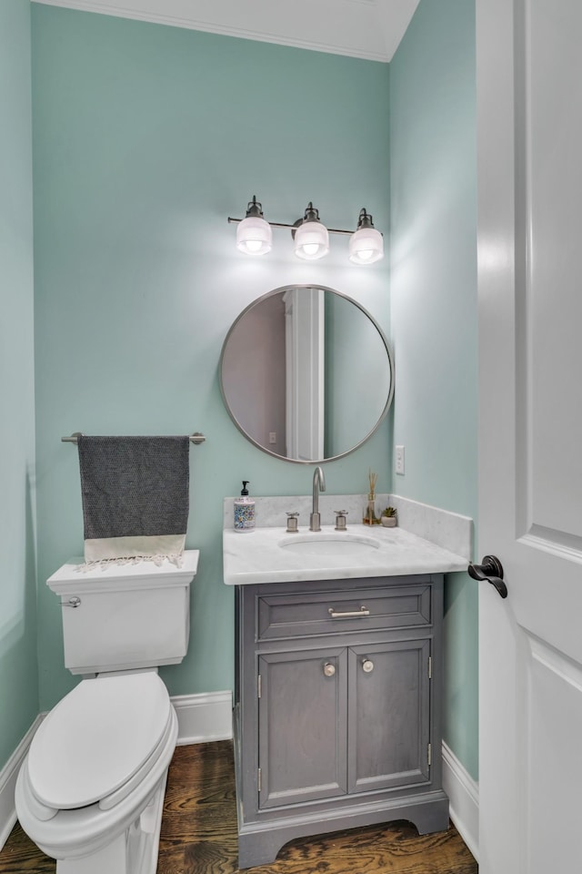 half bath featuring baseboards, vanity, toilet, and wood finished floors