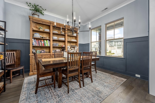 dining space featuring dark wood-style floors, crown molding, a notable chandelier, visible vents, and wainscoting