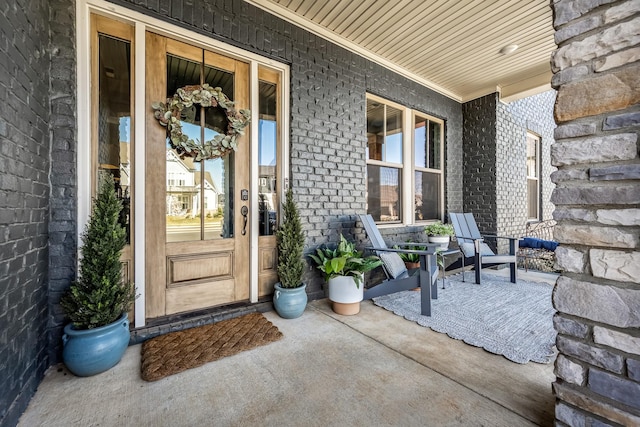 view of exterior entry with a porch and brick siding