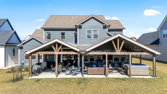 rear view of property with a hot tub, roof with shingles, a lawn, and a patio