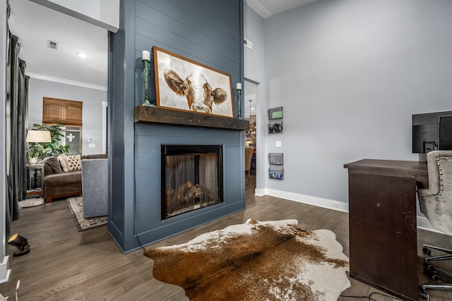 living room with crown molding, visible vents, a large fireplace, wood finished floors, and baseboards