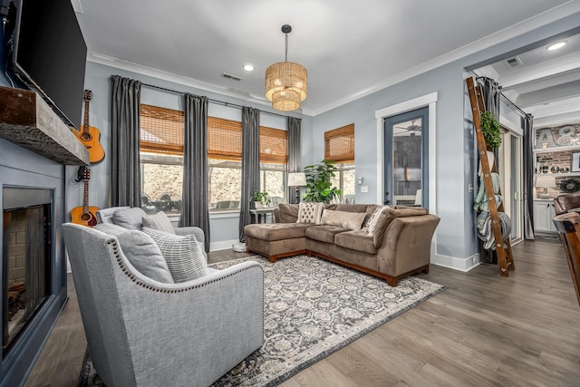 living area with a fireplace, visible vents, wood finished floors, and ornamental molding