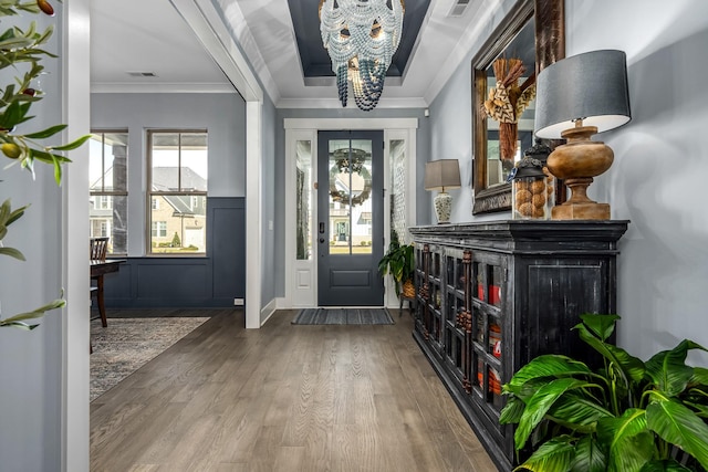 foyer entrance with an inviting chandelier, crown molding, visible vents, and wood finished floors