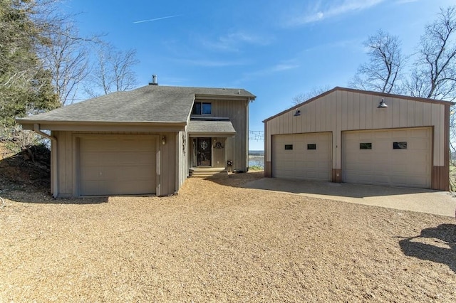 view of front facade featuring a shingled roof, an outbuilding, and a detached garage