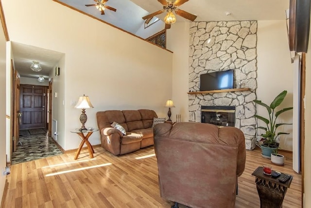 living area featuring ceiling fan, high vaulted ceiling, wood finished floors, and a stone fireplace