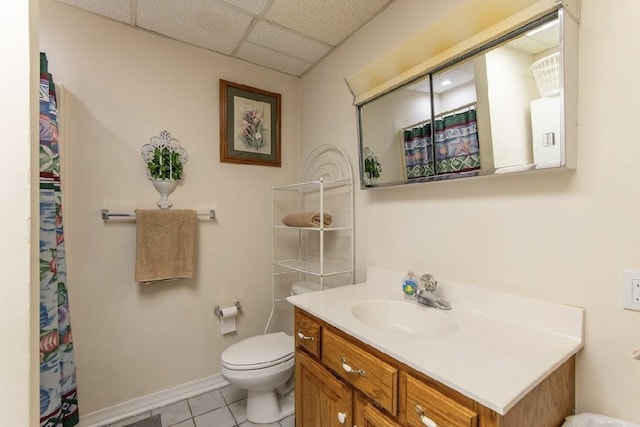 bathroom featuring a paneled ceiling, toilet, vanity, tile patterned flooring, and baseboards