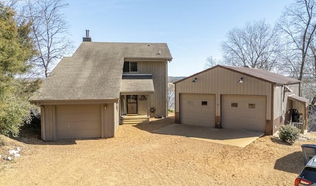 view of front facade featuring a garage, a shingled roof, a chimney, and an outdoor structure