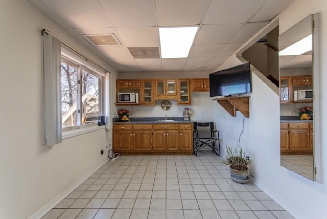 kitchen with white microwave, brown cabinetry, a sink, and visible vents