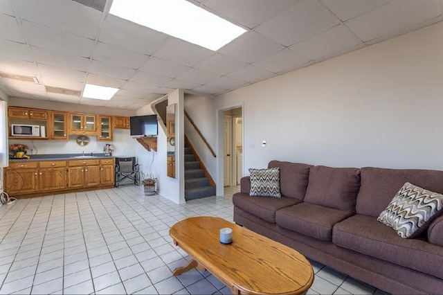 living area with a paneled ceiling, light tile patterned floors, and stairway