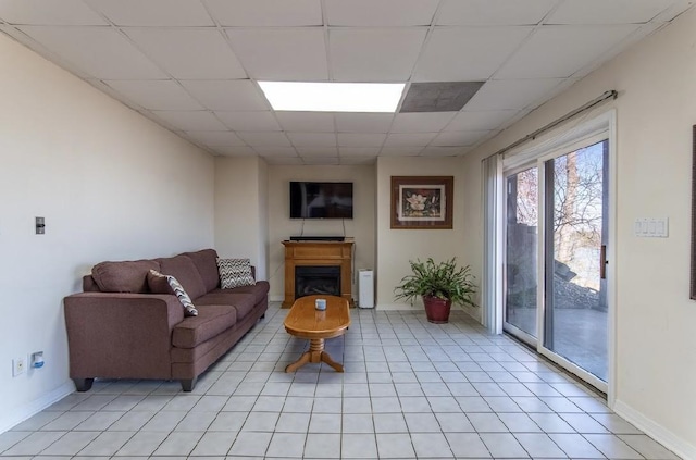 living area featuring a paneled ceiling, a fireplace, baseboards, and light tile patterned floors