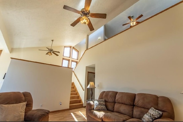 living room featuring a ceiling fan, light wood-type flooring, high vaulted ceiling, and stairway