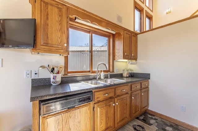 kitchen with dishwashing machine, a sink, baseboards, brown cabinets, and dark countertops