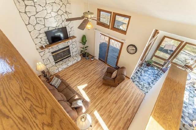 living area featuring a ceiling fan, wood finished floors, and a stone fireplace