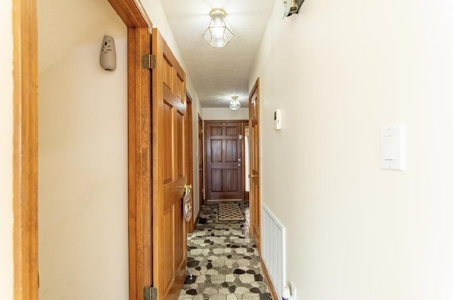 hall with visible vents, a textured ceiling, and light floors