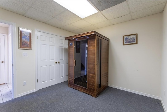 unfurnished bedroom with carpet, a closet, a drop ceiling, and baseboards