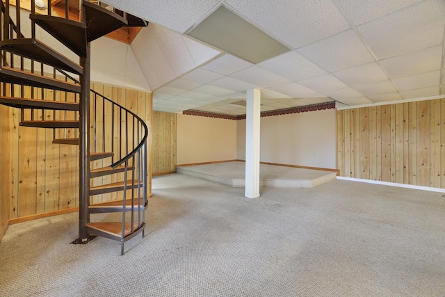 finished basement featuring stairway, carpet, a drop ceiling, and wooden walls