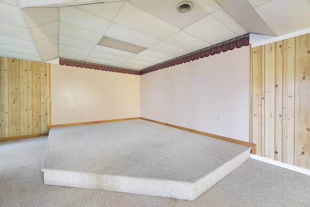 spare room with a drop ceiling, carpet flooring, visible vents, and wooden walls