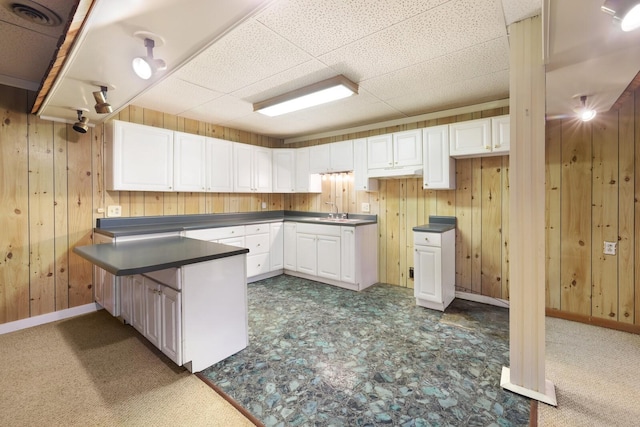 kitchen with a peninsula, wood walls, dark countertops, and white cabinets