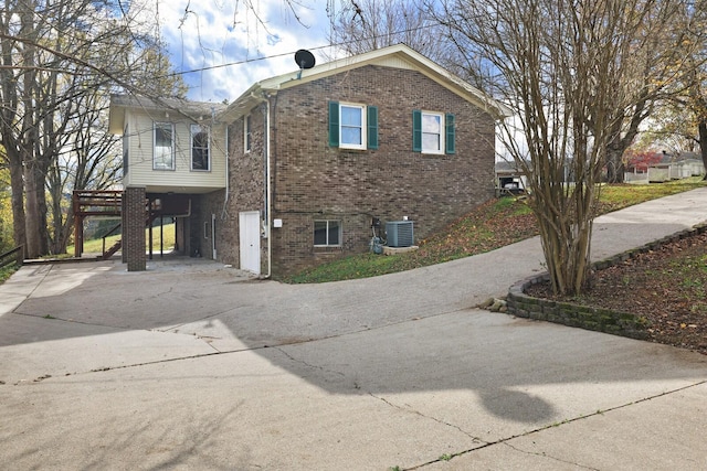 view of side of home with a carport, brick siding, driveway, and central air condition unit