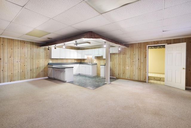 basement with wood walls, baseboards, a drop ceiling, and light colored carpet