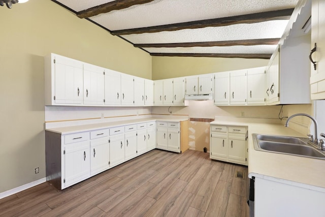 kitchen with vaulted ceiling with beams, a sink, a textured ceiling, wood finished floors, and under cabinet range hood