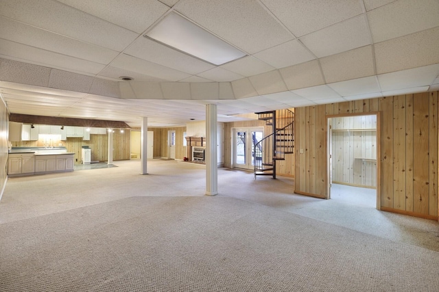 basement featuring light carpet, wood walls, stairway, and a paneled ceiling