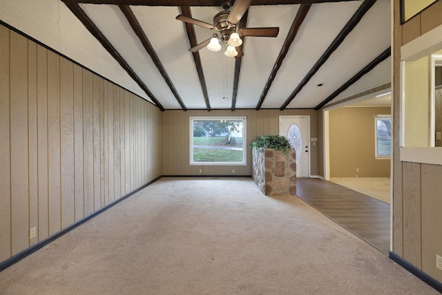 unfurnished living room with vaulted ceiling with beams, carpet floors, a ceiling fan, and wooden walls