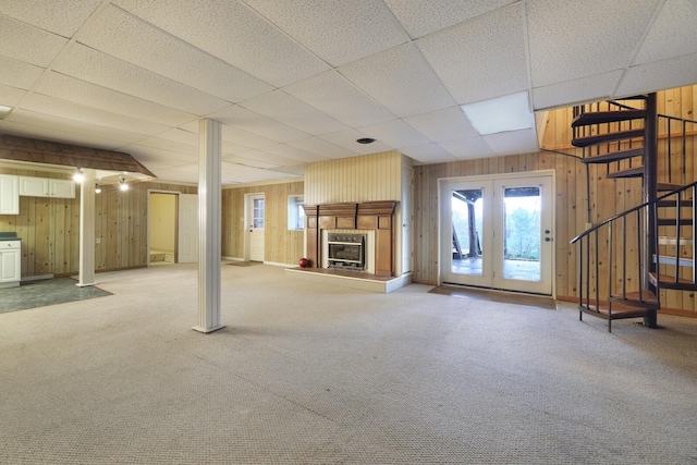 unfurnished living room with wooden walls, a glass covered fireplace, light carpet, and stairway