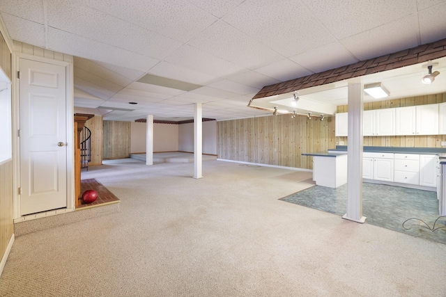 finished basement with wood walls, stairway, a drop ceiling, and light colored carpet