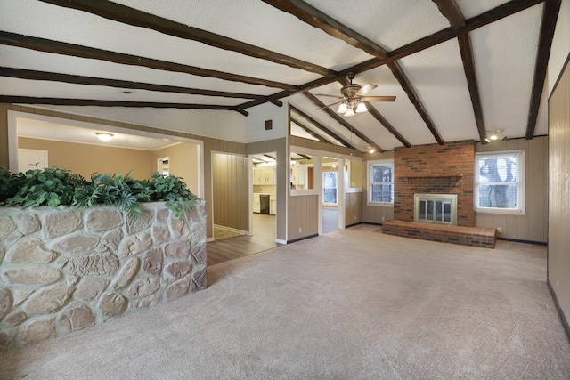 unfurnished living room with lofted ceiling with beams, carpet floors, a fireplace, and a ceiling fan