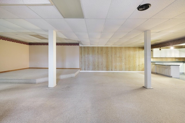 finished below grade area featuring a paneled ceiling, light colored carpet, wooden walls, and baseboards