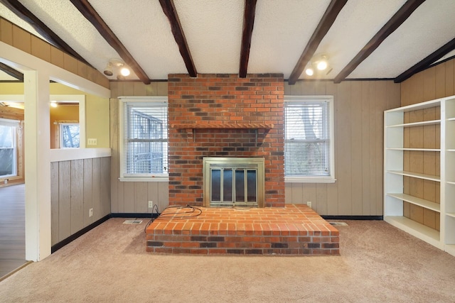 unfurnished living room featuring a wealth of natural light, a brick fireplace, a textured ceiling, and beam ceiling