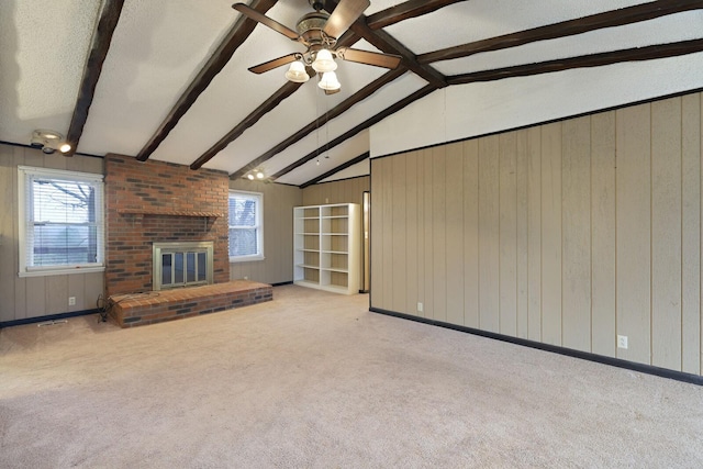 unfurnished living room with lofted ceiling with beams, a brick fireplace, carpet flooring, and wood walls