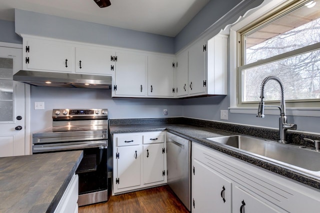 kitchen with under cabinet range hood, stainless steel appliances, a sink, white cabinets, and dark countertops