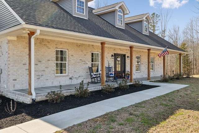 view of front facade featuring a porch, brick siding, and roof with shingles